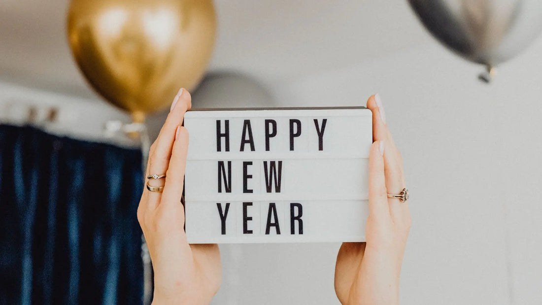 The photo shows a sign with the text "Happy New Year," likely held by a woman. Balloons can be seen in the background.